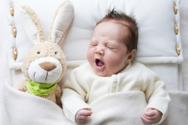 Yawning newborn baby near toy rabbit