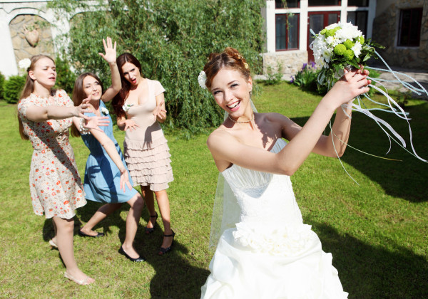 Young bride in white wedding dress throws a bouquet of flowers to bridesmaids