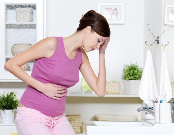 Pregnant woman with strong pain of stomach and nausea sitting in bathroom