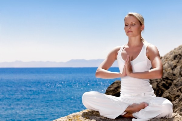 Красиво позитивно момичешко облекло в бяло седи на морския бряг на скалата и медитира в йога поза