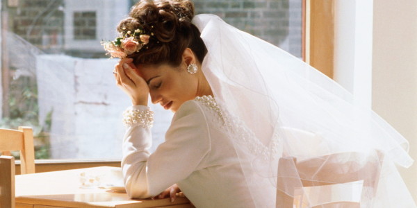 Bride sitting alone at table, head in hands