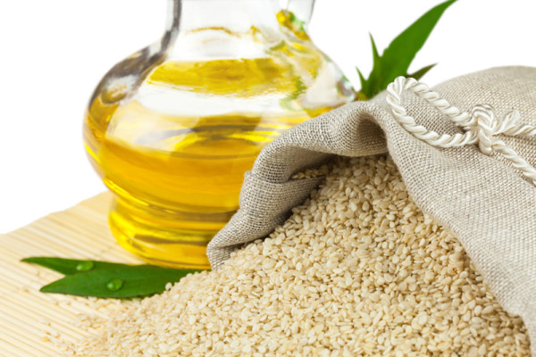 Sack of sesame seeds and glass bottle of oil on mat
