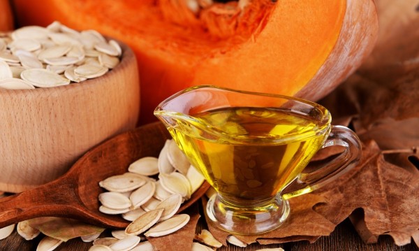 Pumpkin seed oil in glass sauce-boat and fresh pumpkin on wooden background