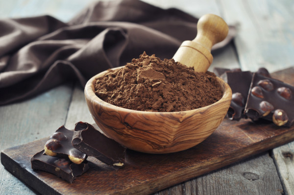Carob powder in bowl with chocolate pieces on wooden background