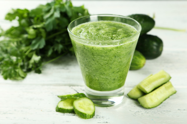 Glass of cucumber juice on white wooden background