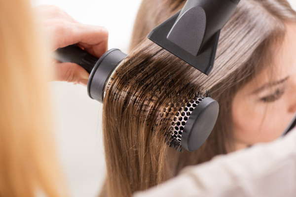 Drying long brown hair with hair dryer and round brush. Close-up.