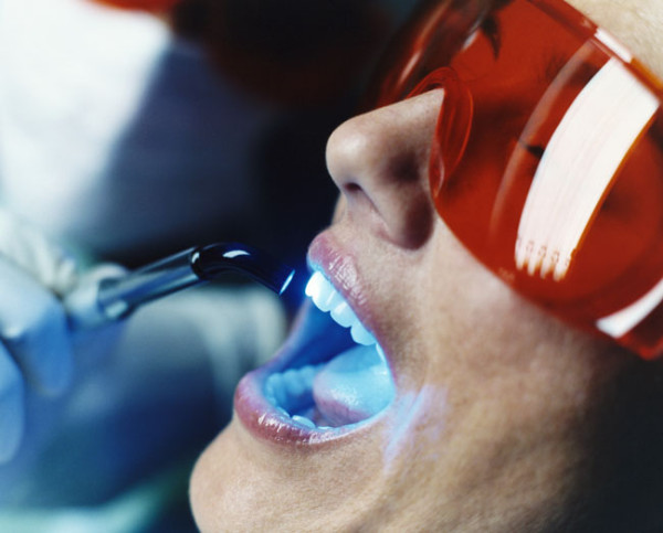 Зъболекар, преглеждащ жена's Teeth With Ultraviolet Light