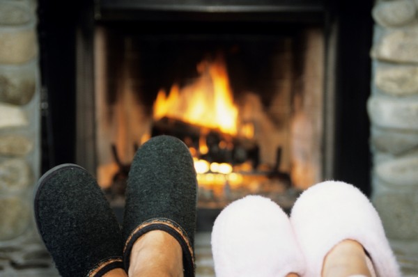 Two pairs of feet with slippers in front of fireplace, close-up, low section