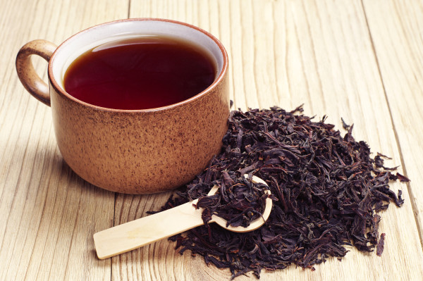 Црн чај во чаша и суви лисја на дрвена позадина