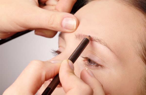 Stylist is penciling eyebrow for young girl