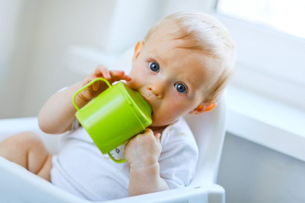 Lovely baby  sitting in chair and drinking from cup